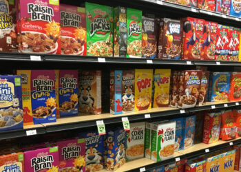 Grocery store shelves, filled with colorful cereals, like Raisin Bran, Apple Jacks, Pops, and Froot Loops.