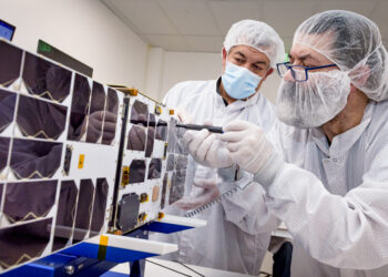 Mario Perez, back, holds a deployable solar panel as Craig Turczynski, left, secures it to the Advanced Composite Solar Sail System (ACS3) spacecraft in the Integration Facility of NASA Ames Research Center.