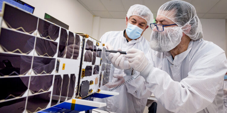 Mario Perez, back, holds a deployable solar panel as Craig Turczynski, left, secures it to the Advanced Composite Solar Sail System (ACS3) spacecraft in the Integration Facility of NASA Ames Research Center.